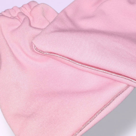 A close-up of a pair of Fairy Floss Pink knit stirrup socks with elasticized cuffs, and Baby Pink shimmer piping, shown overlapping on a light lavender background.
