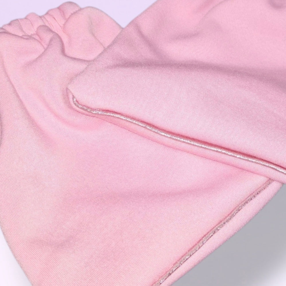 A close-up of a pair of Fairy Floss Pink knit stirrup socks with elasticized cuffs, and Baby Pink shimmer piping, shown overlapping on a light lavender background.